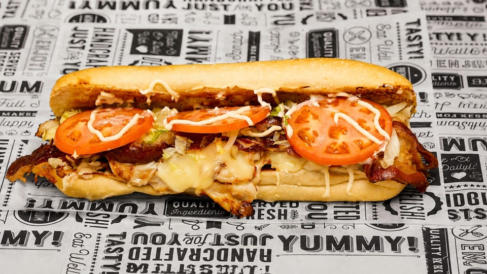 A delicious sub sandwich filled with melted cheese, meat, tomatoes, and sauce on branded paper.