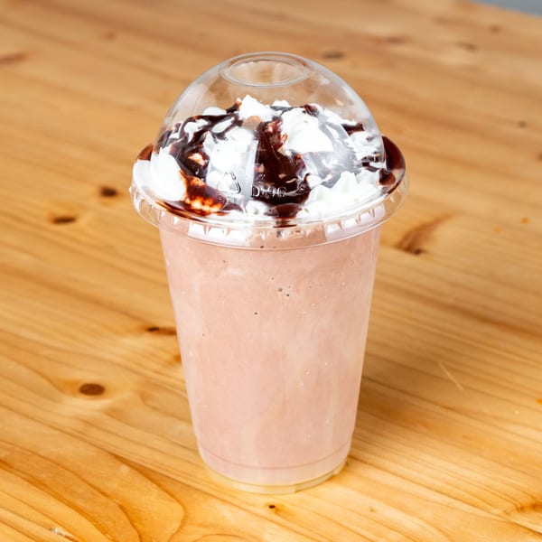 Chocolate milkshake with whipped cream and chocolate syrup in a plastic cup on a wooden table.
