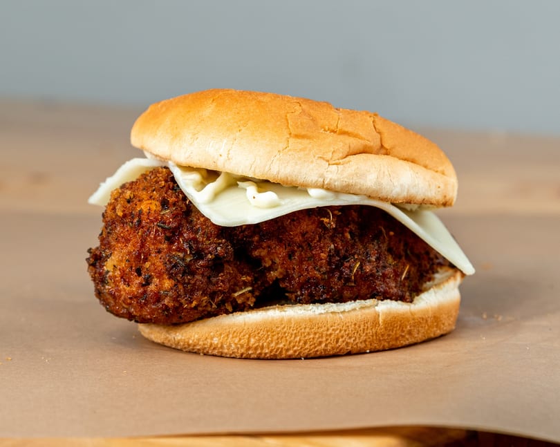Crispy fried chicken sandwich with melted white cheese and mayonnaise on a toasted bun.