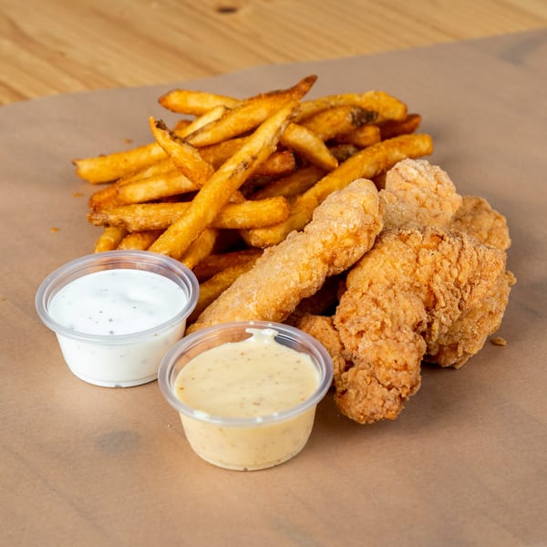 Crispy fried chicken tenders and golden french fries with two dipping sauces on brown paper.