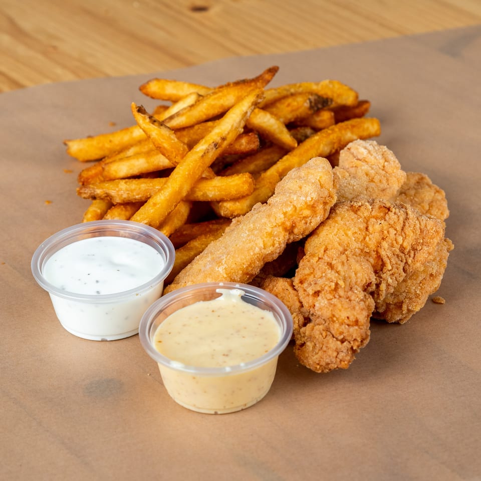 Crispy fried chicken tenders and golden french fries with two dipping sauces on brown paper.