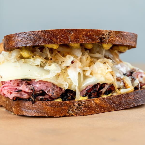 A close-up of a hearty pastrami sandwich on toasted rye with melted cheese, sauerkraut, and mustard.