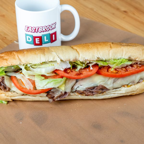 Eastbrook Deli sub sandwich with roast beef, melted cheese, lettuce, and tomatoes, next to a branded mug.