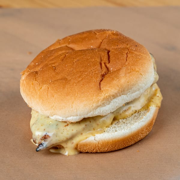 A grilled chicken sandwich with melted cheese and mustard on a toasted bun.