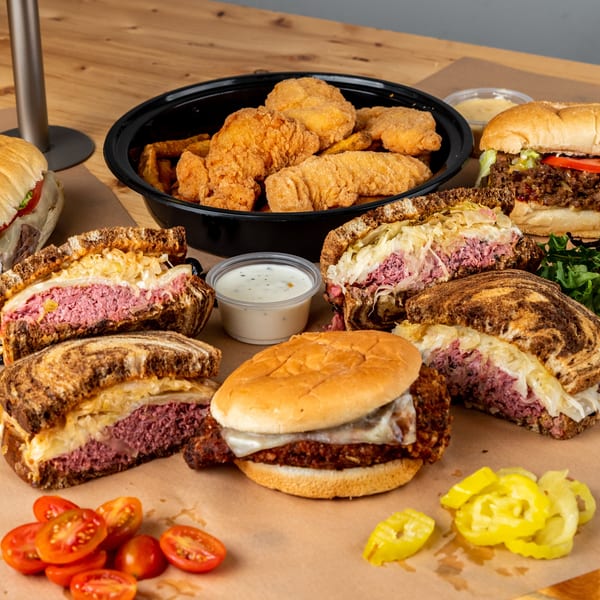 Assortment of sandwiches, including Reubens, subs, and a fried chicken sandwich, with fries and sauces.
