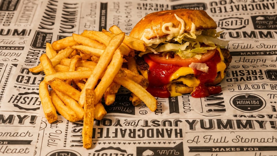 A double cheeseburger with lettuce, tomato, ketchup, and mayonnaise, next to a pile of french fries.