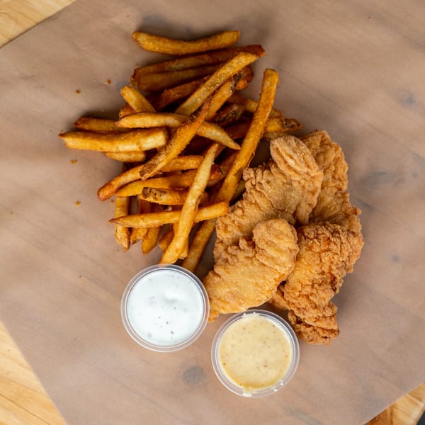 Crispy chicken tenders and golden french fries with two dipping sauces on a brown paper-lined tray.