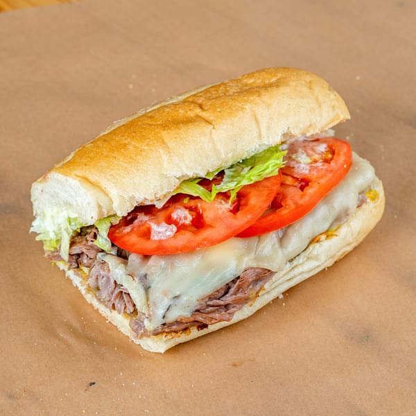 Roast beef sub sandwich with melted cheese, lettuce, and sliced tomatoes on a brown paper.