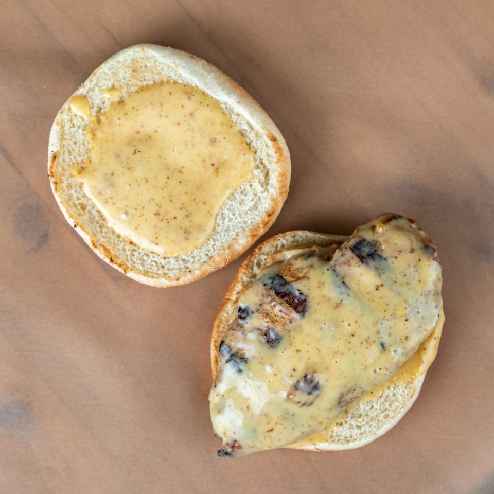 Top-down view of an open chicken sandwich with creamy sauce on a bun.